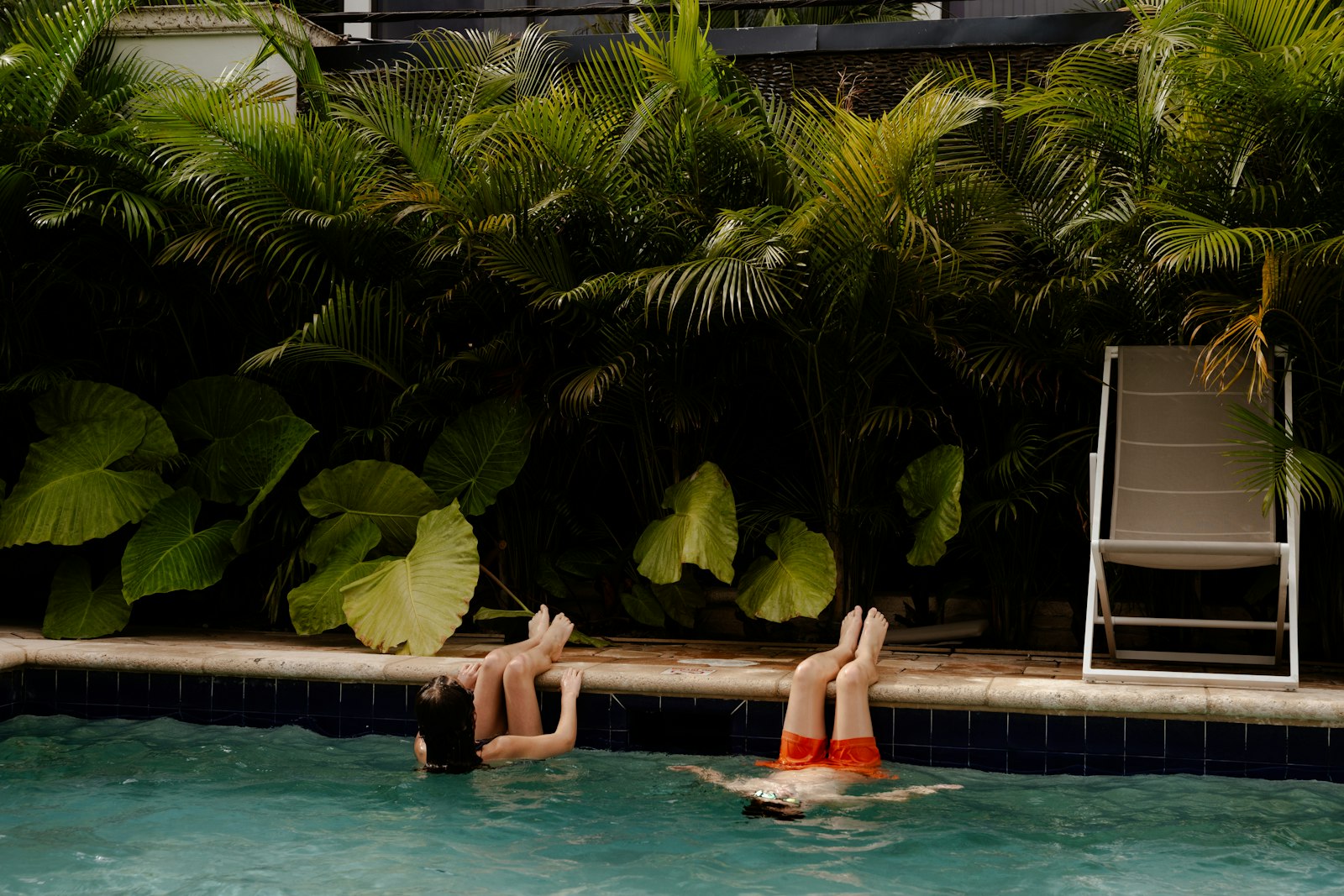 Two people swimming in a pool with lush greenery.